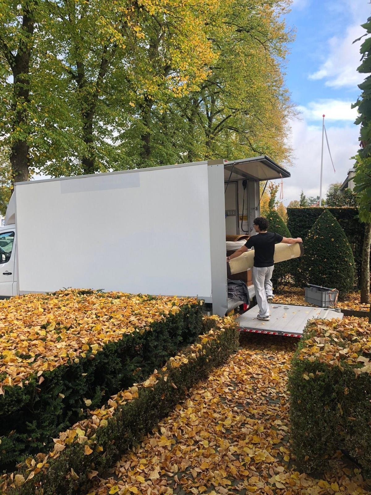 Verhuizer draagt een opgerold tapijt de verhuiswagen in